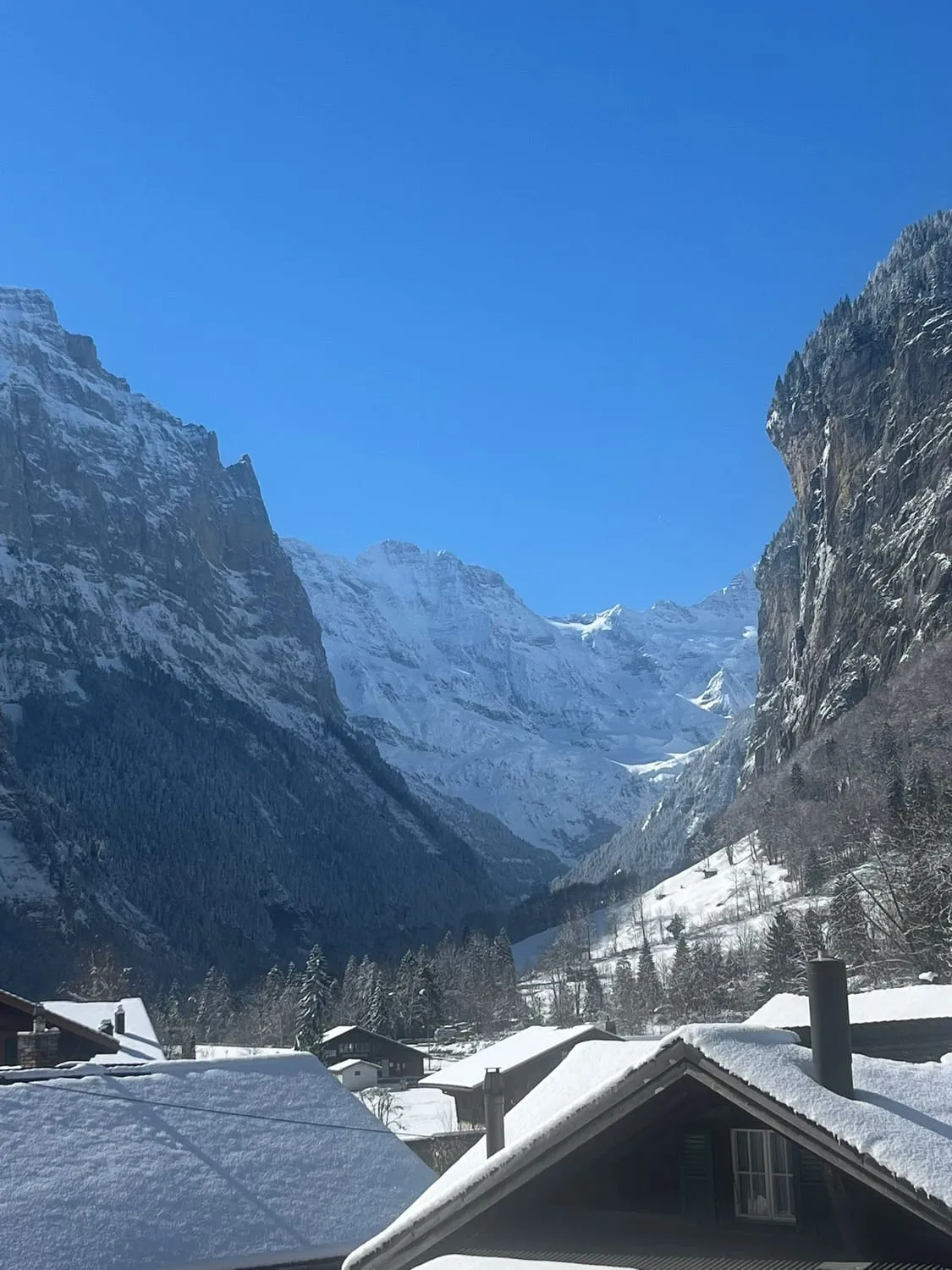Snow covered roofs below a steep mountain wall at dusk.