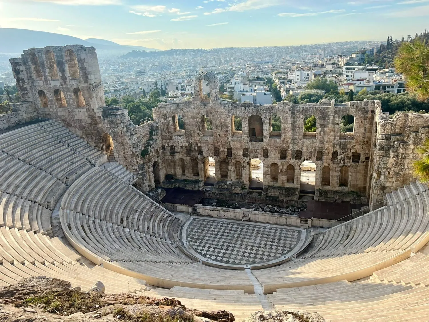 A stone amphitheatre seen from above, a city spreading out behind it.