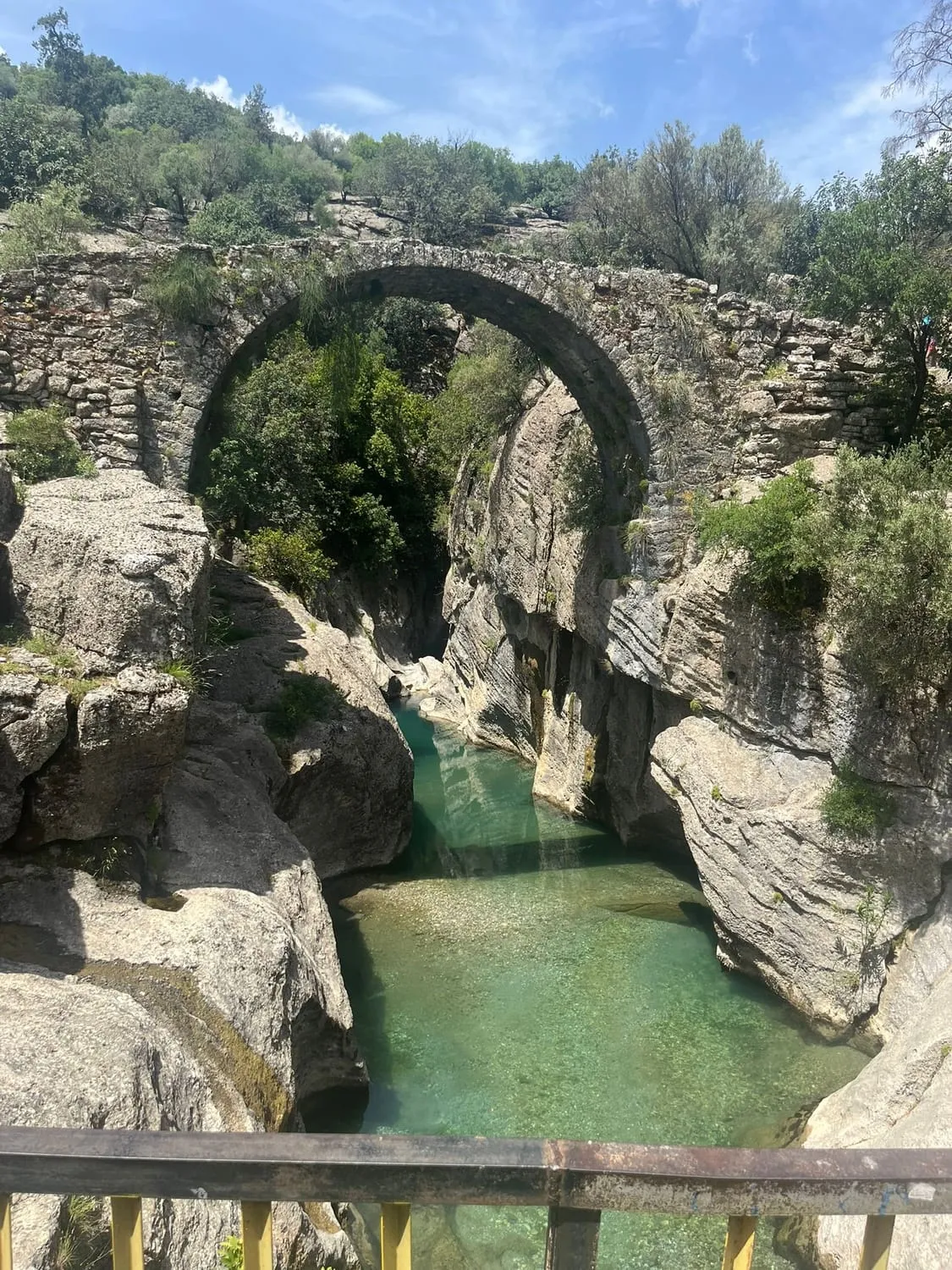 An old stone arch bridge over a still green pool in a narrow gorge.