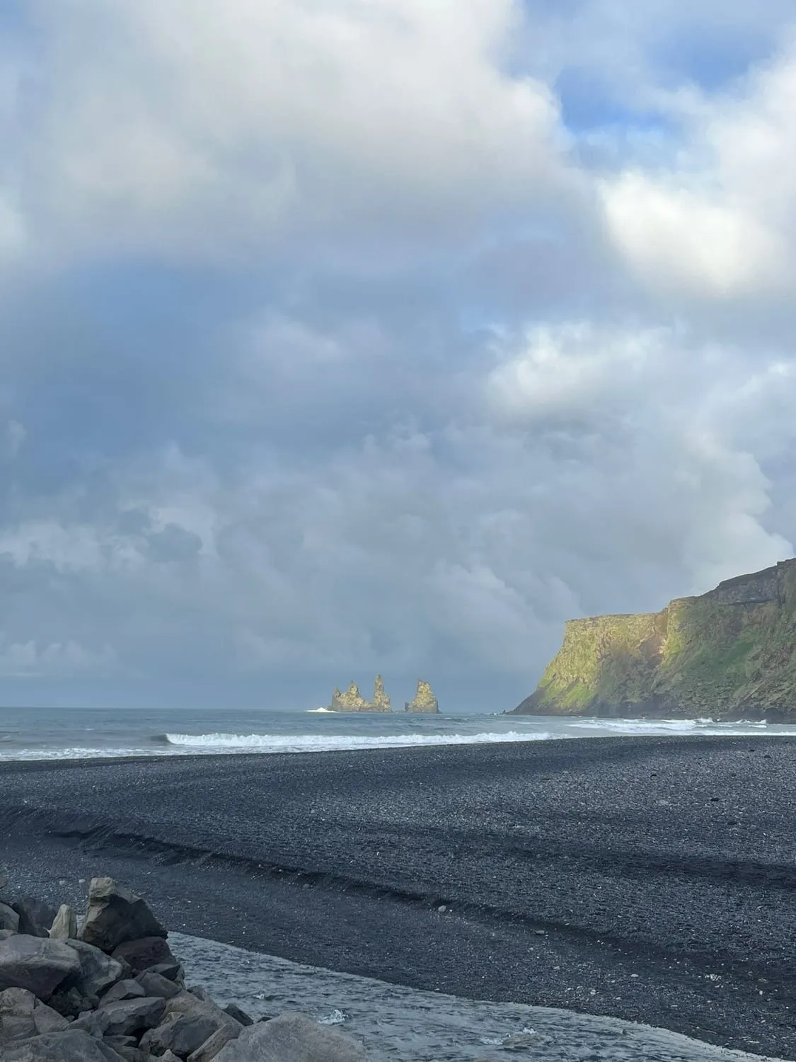 A black beach running out to a headland half lost in sea mist.