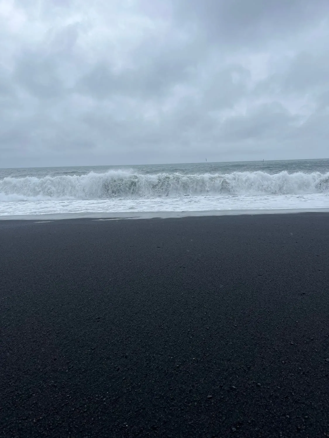 Surf breaking in a long white line onto flat black sand.