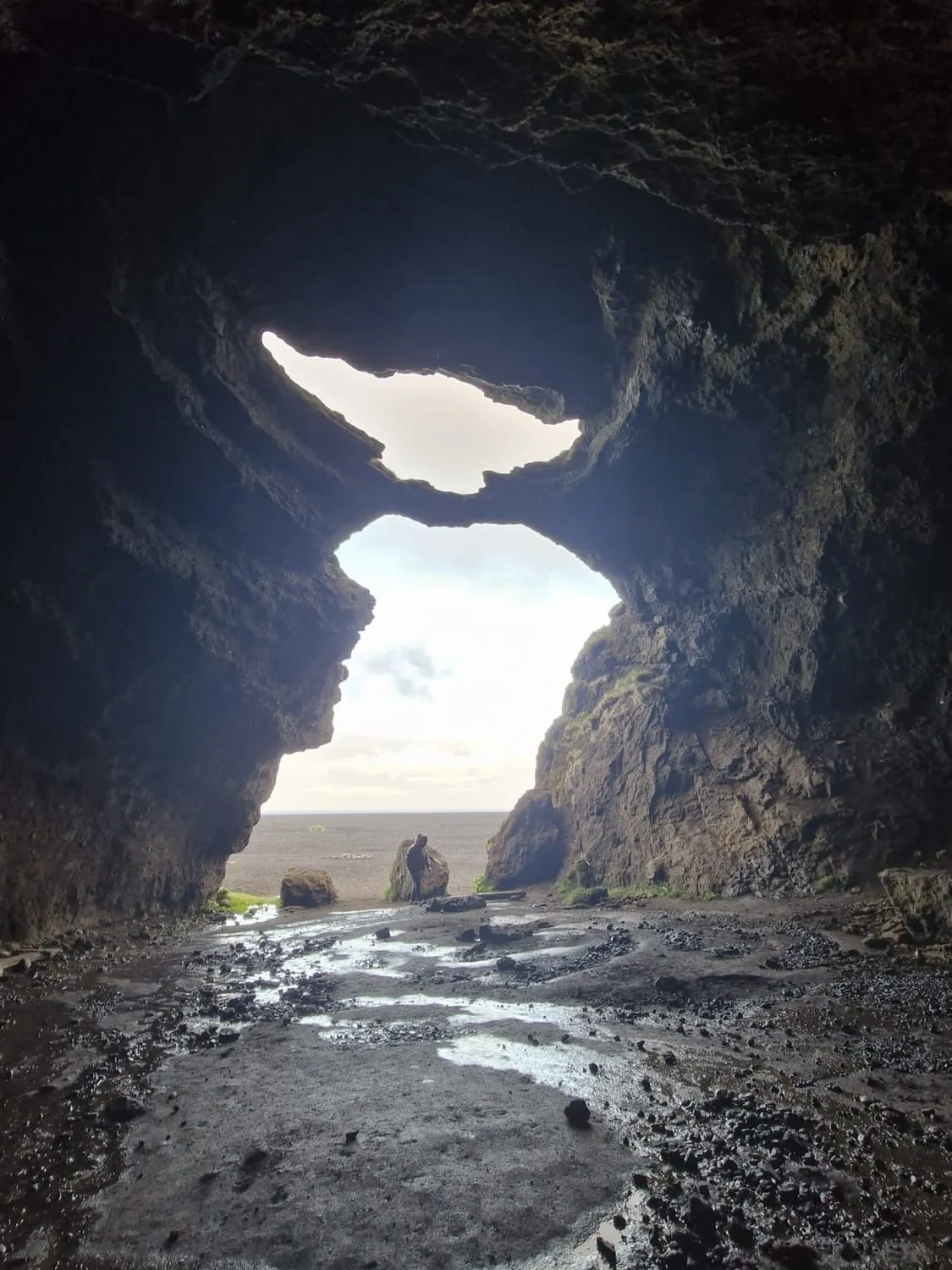 The mouth of a cave in silhouette, opening onto a bright wet plain.