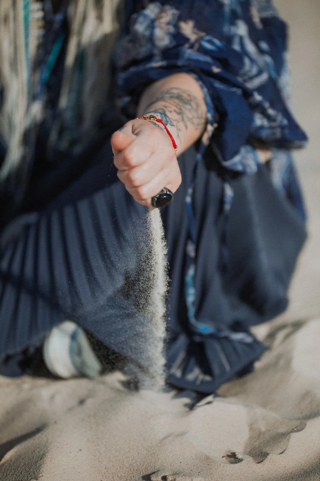 A hand opening above a dune, letting a fine stream of sand fall away.