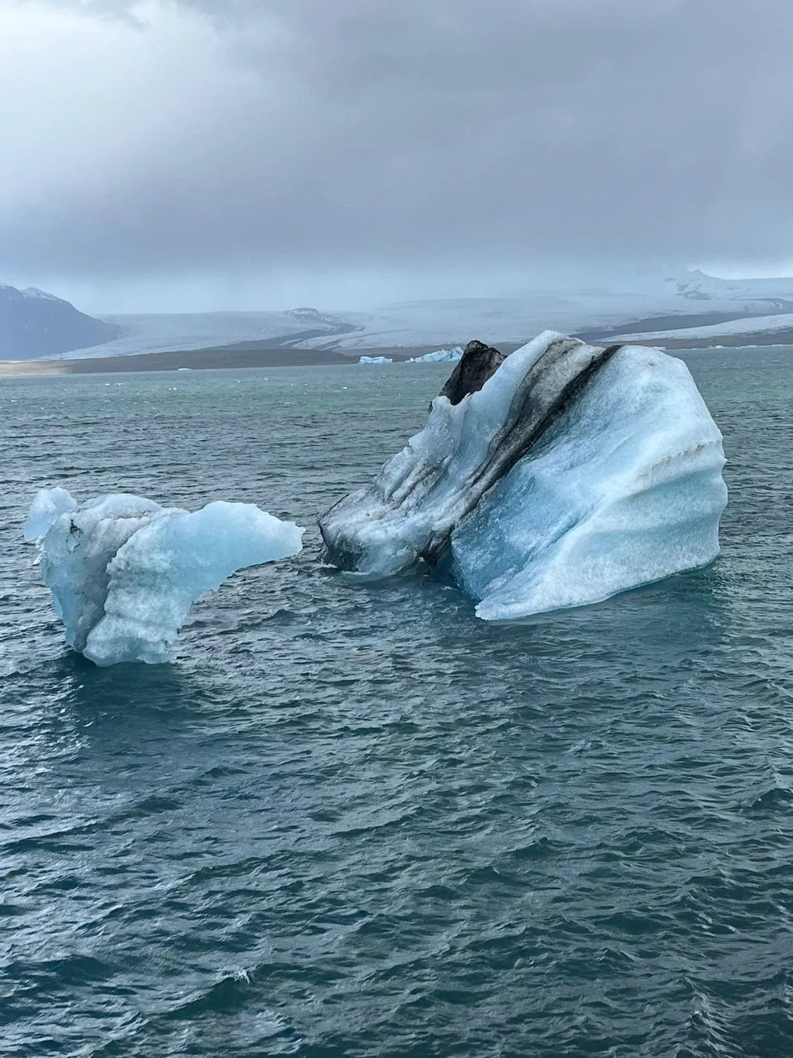 Icebergs drifting in a still grey lagoon.
