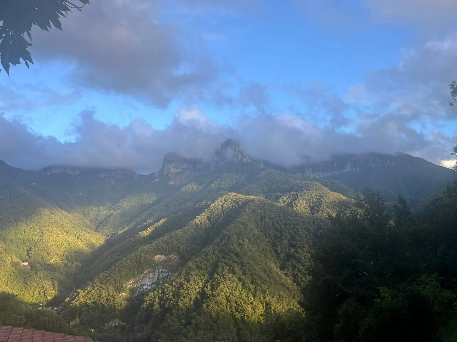 Steep green mountains half covered by low cloud, sunlight on the slopes.