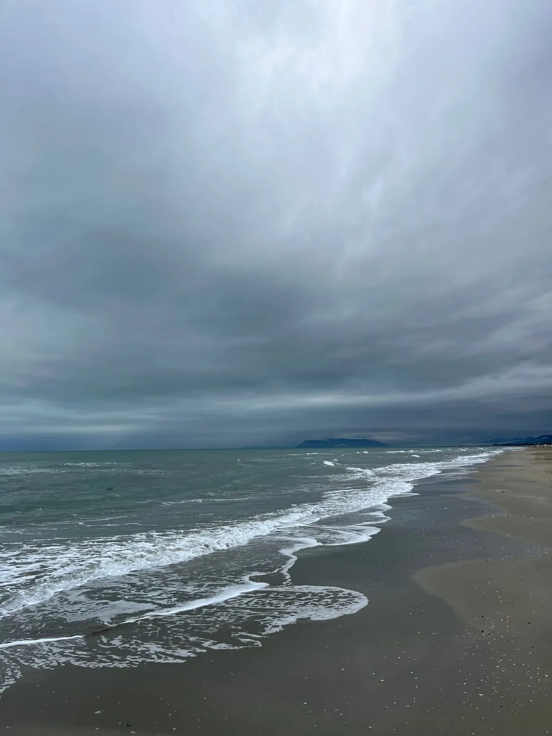 Foam sliding up a wide grey beach, a low headland in the distance.