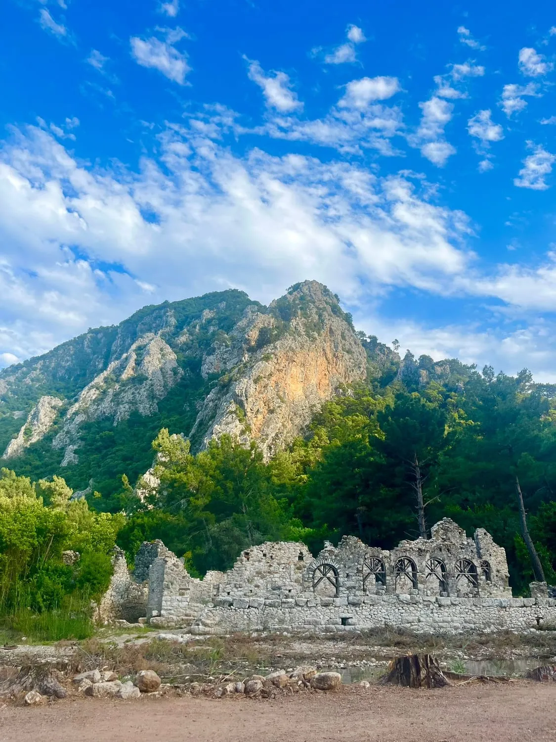 Ruined walls on a wooded hillside beneath a bare mountain ridge.