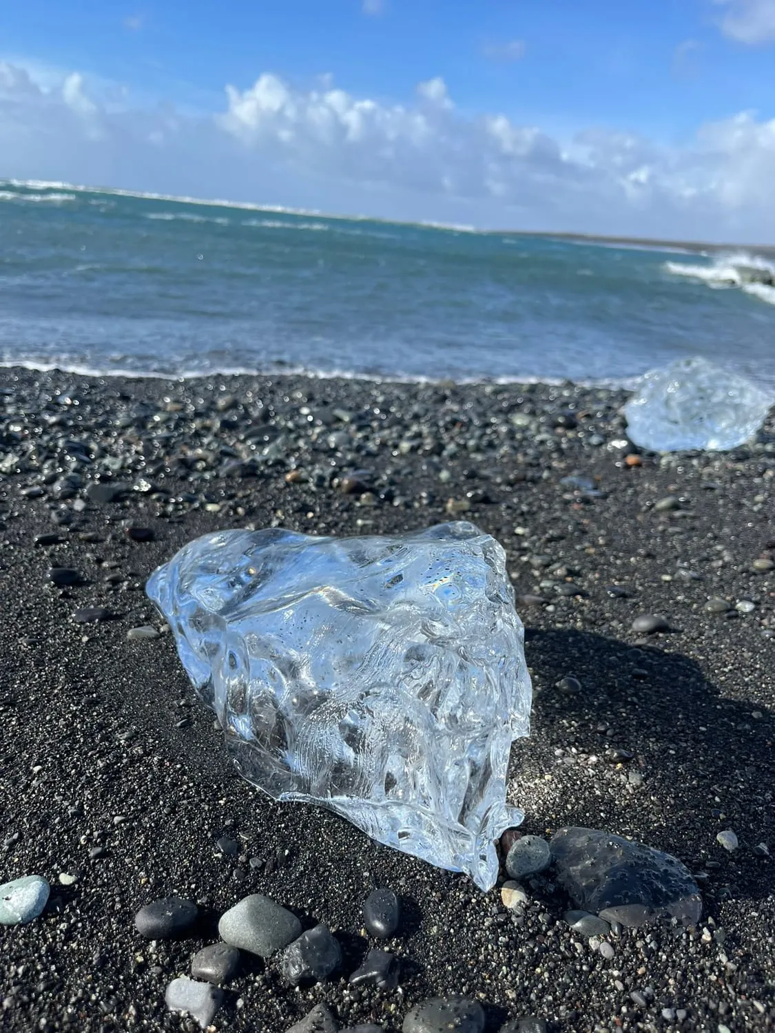 A block of clear glacier ice resting on a black pebble beach.