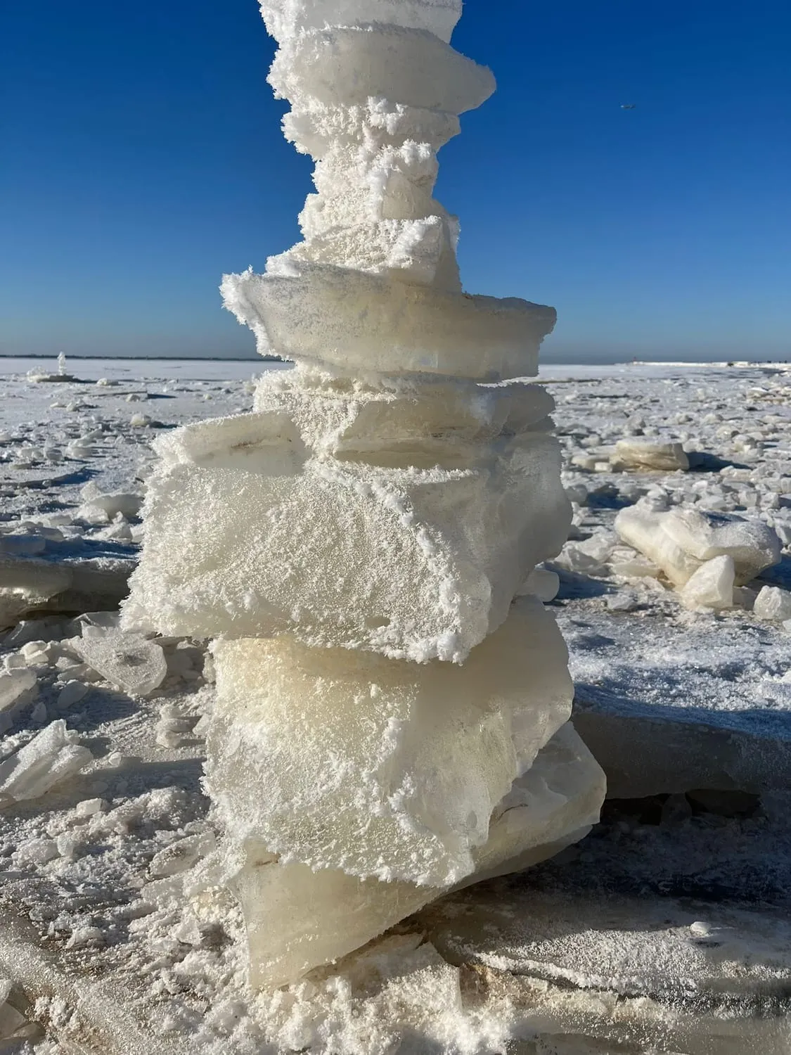 Slabs of pale ice stacked into a column on a frozen shore.