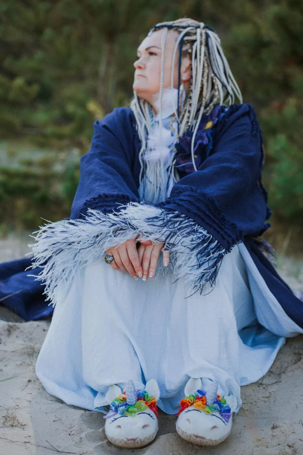 Liana sitting on sand in a deep blue wrap, looking out to one side.