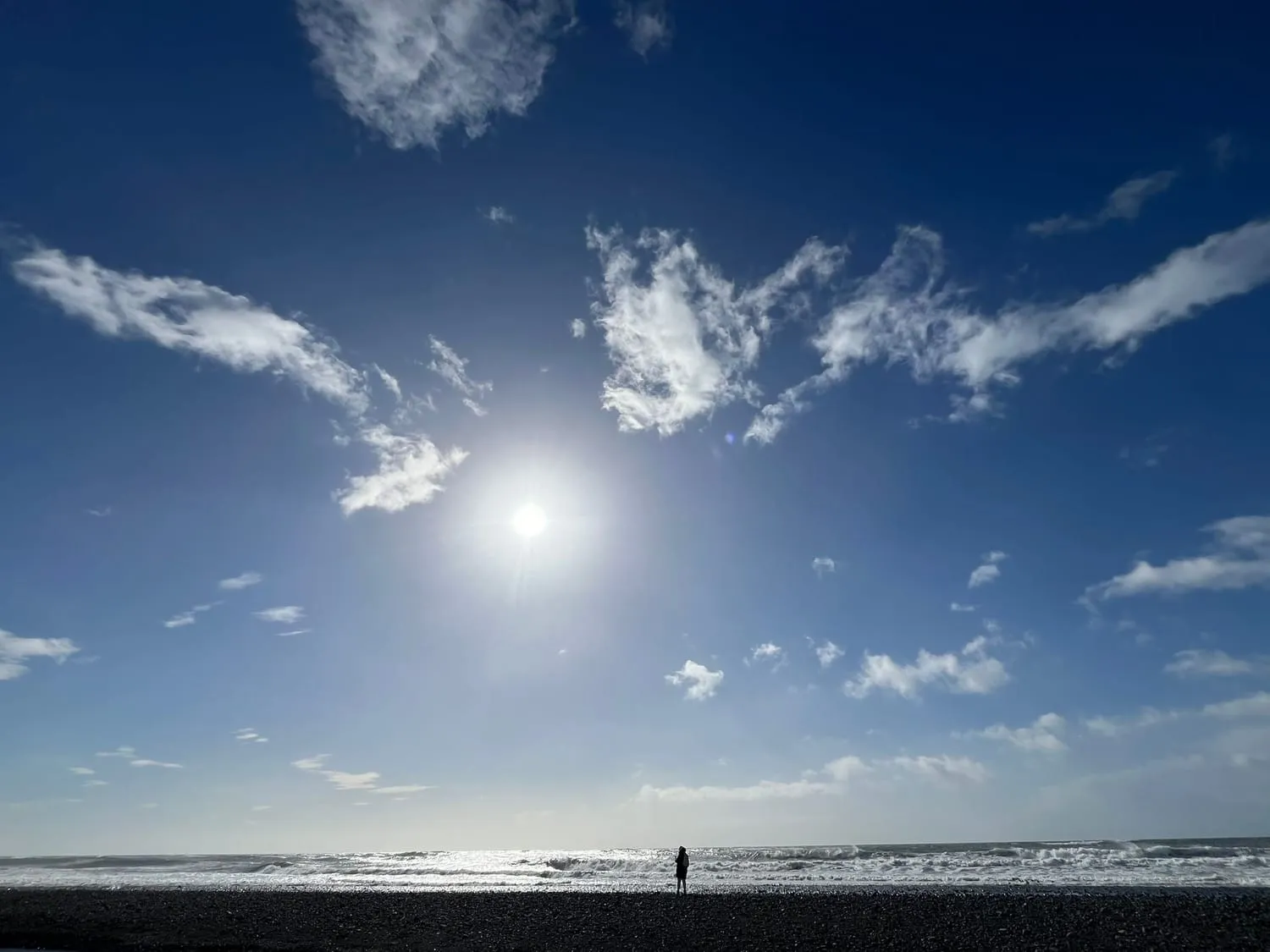 A low sun through high cloud over wet sand, one small figure far off.