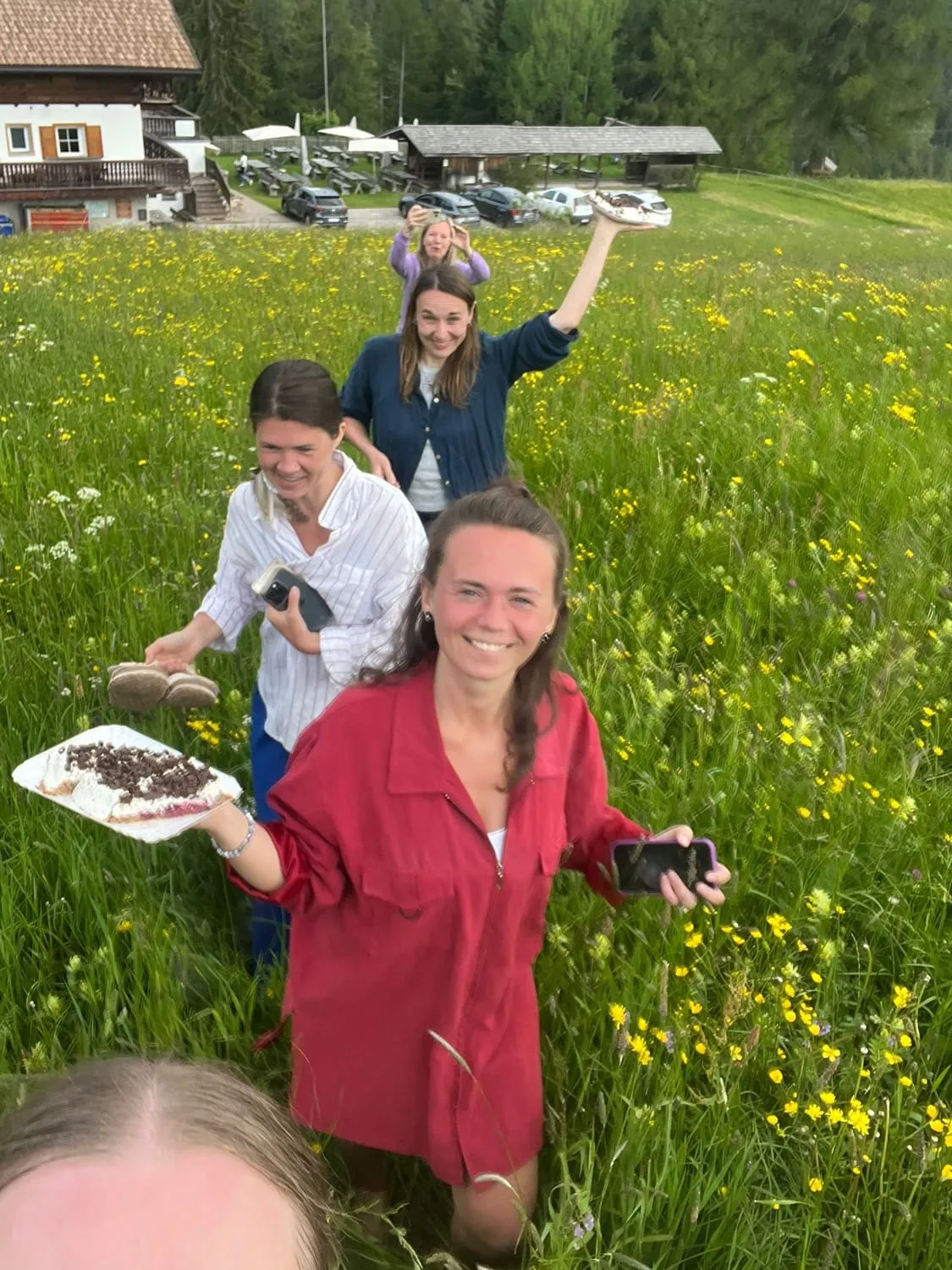Women standing in a flowering meadow on a bright day, one holding a plate.