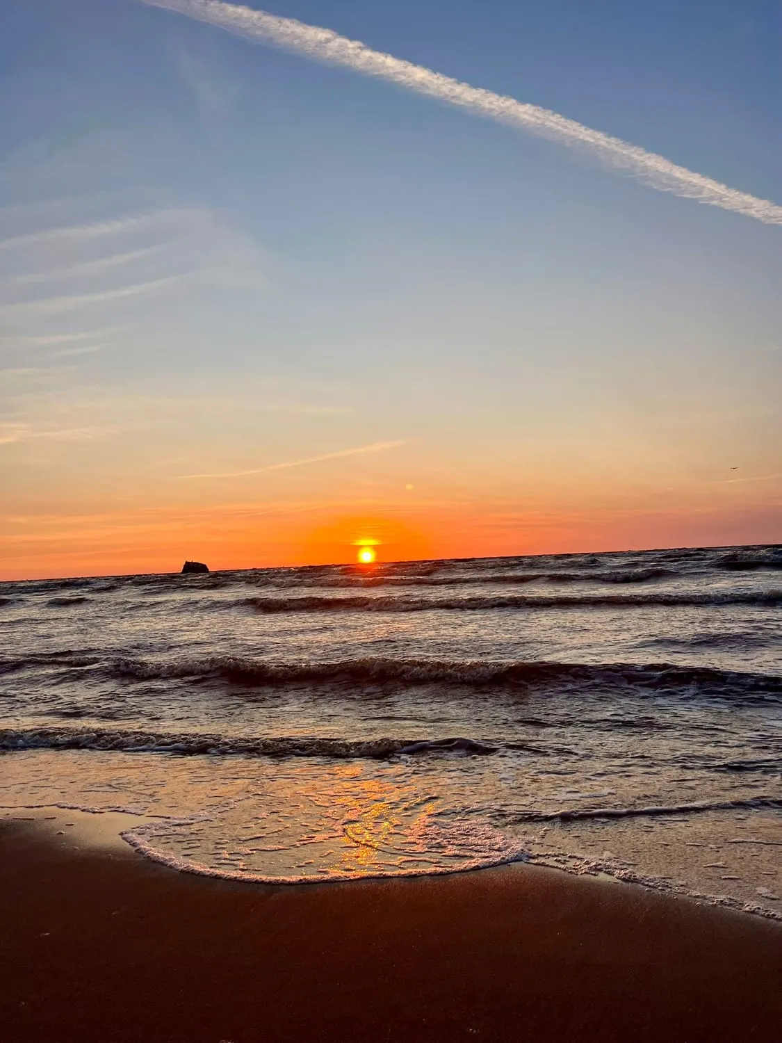 An orange sun almost touching the horizon, its light across the water.