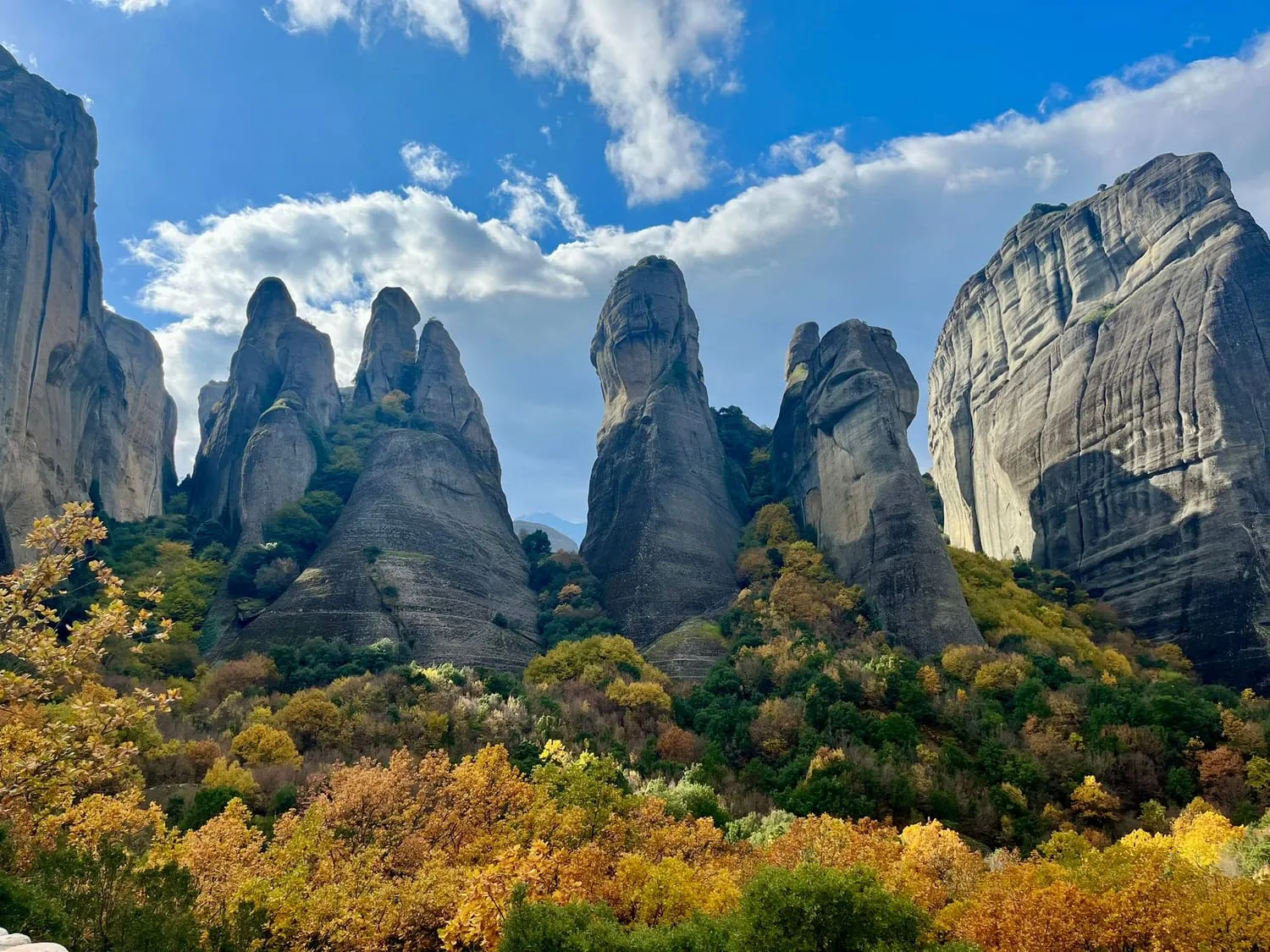 Enormous rounded rock pillars rising out of autumn woodland under a blue sky.