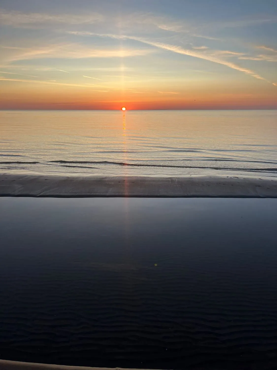 A low sun over a flat sea, a vertical pillar of light rising from it.