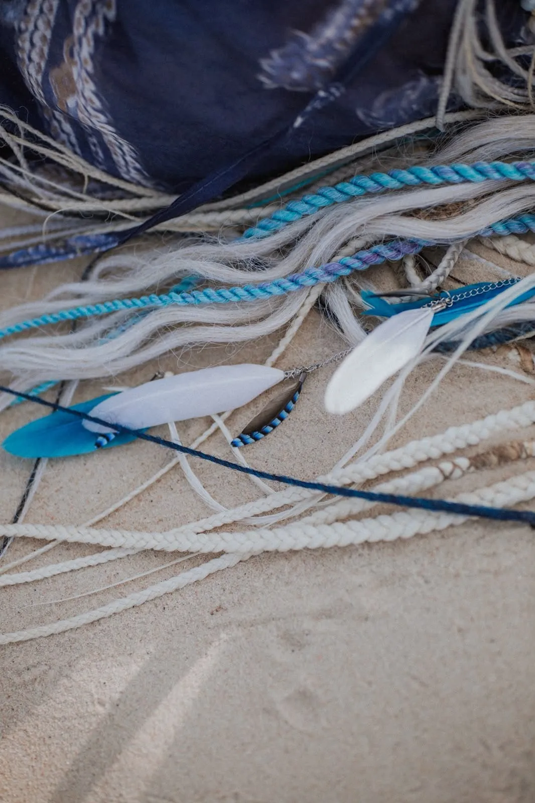 A close view of Liana's braided hair, feathers and cords lying on sand.