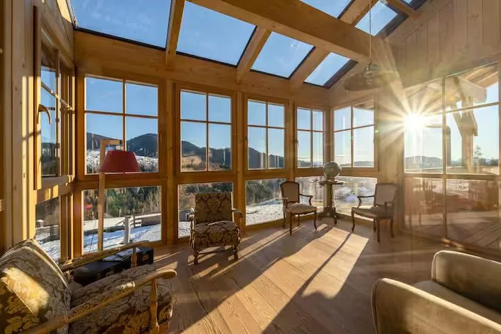 A wooden room with a glass roof and low sun coming through the windows, chairs set around it.