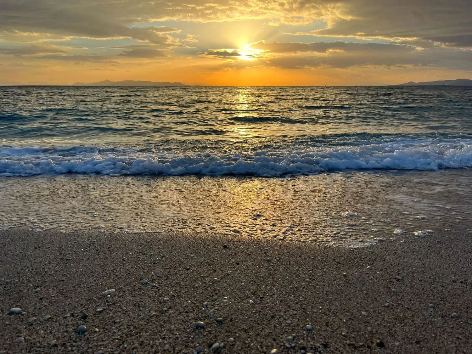 The sun setting into the sea, small waves running up onto the sand.