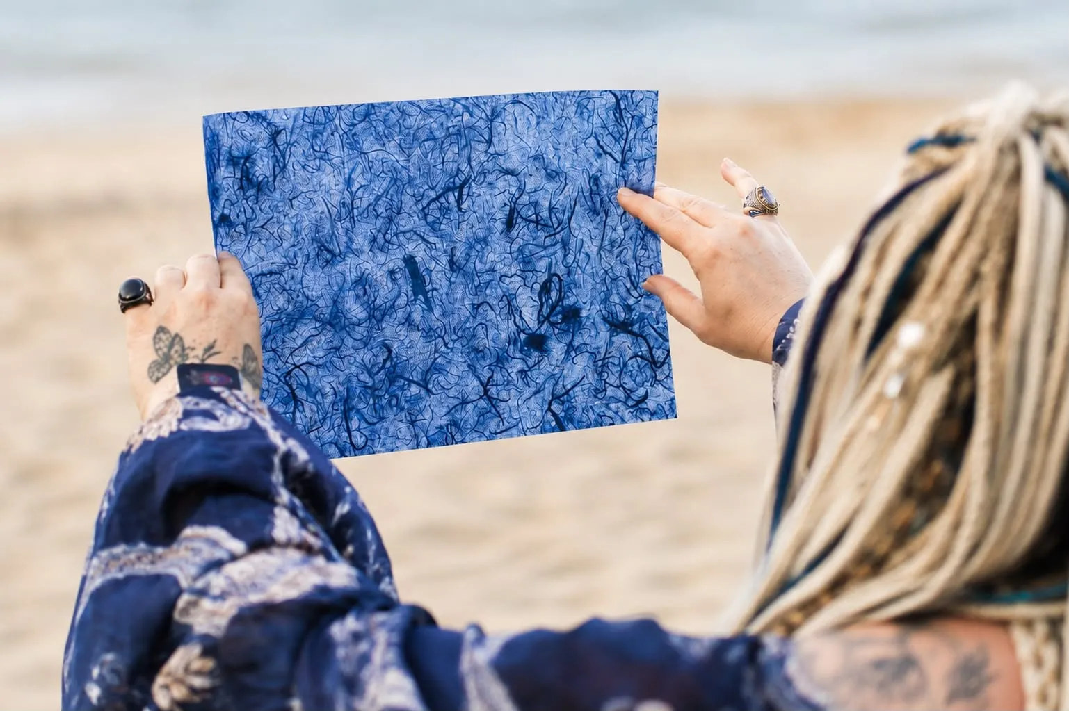 Liana holding a blue, densely fibrous sheet up in front of her on the shore.