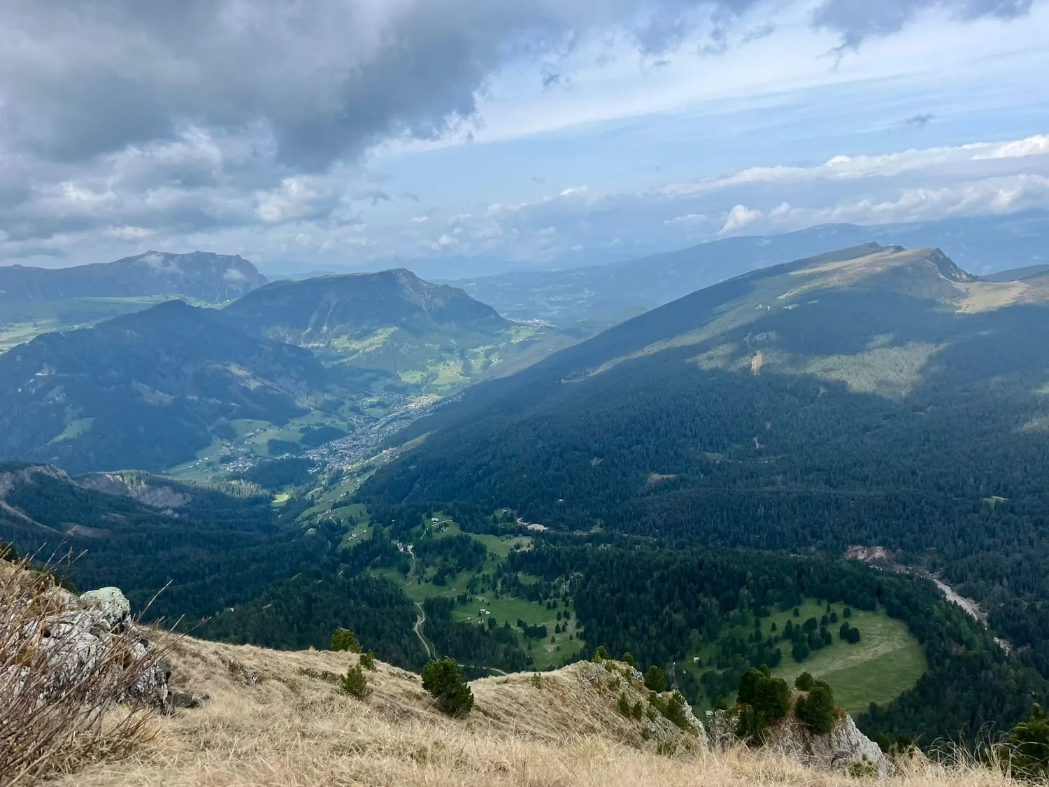 A green valley seen from a high ridge, forested slopes on both sides.